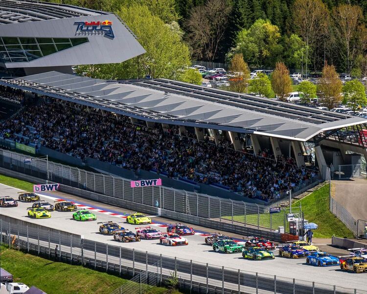 Ein spannendes Autorennen mit mehreren Fahrzeugen vor einer jubelnden Zuschauertribüne in Österreich.