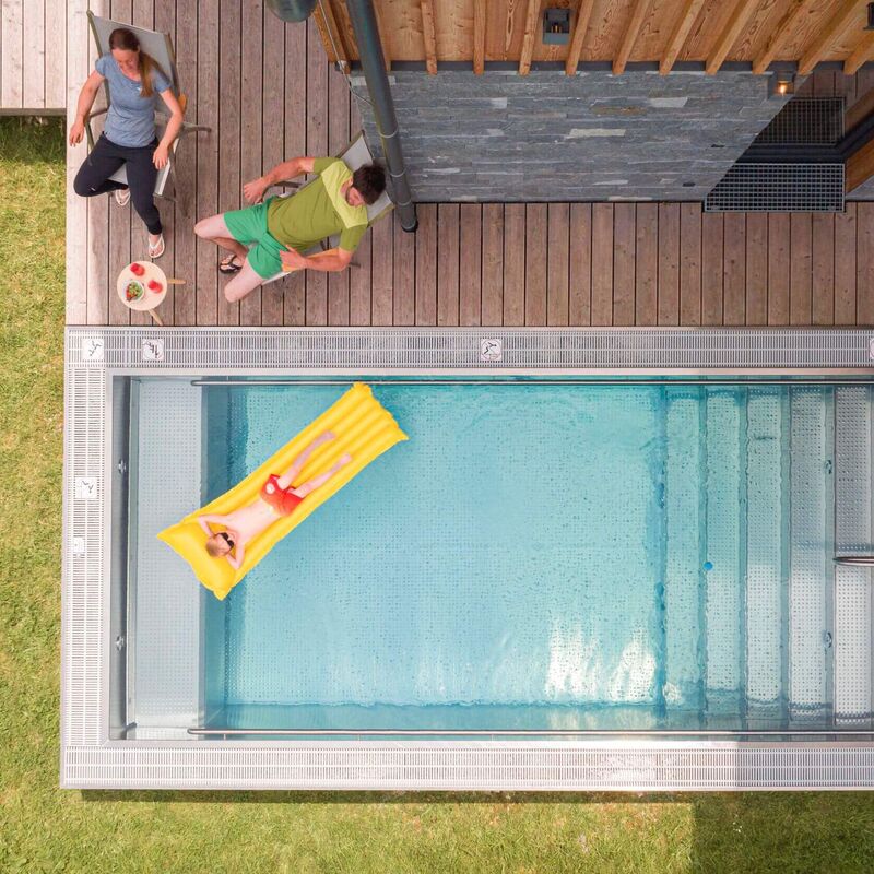 Eine Frau entspannt auf einer Luftmatratze, während ein Mann neben einem Pool auf der Terrasse sitzt.
