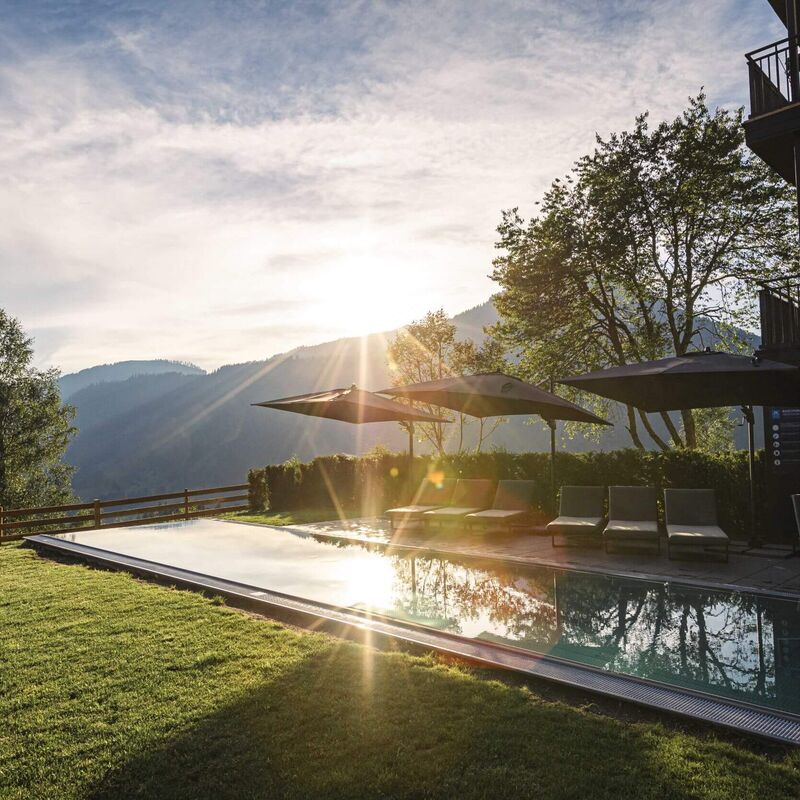 Outdoor pool with sun loungers at sunset in the mountains