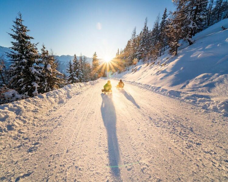 2 tobogganists ride their sledges down the toboggan run into the sunset.