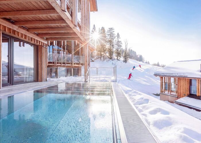 Verschneites Ferienhaus mit privatem Pool und Skifahrer im Hintergrund