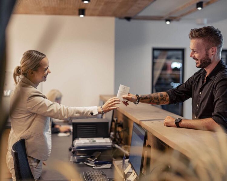 A receptionist hands her guest a guest card.