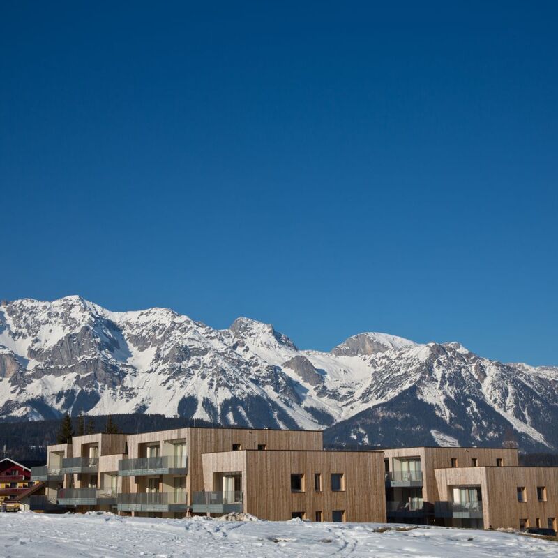 Moderne Gebäude im Schnee vor majestätischen Alpenbergen unter klarem, blauem Himmel.