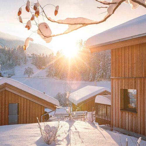 Holzchalets der Bergeralm Chalets im Schnee bei tief stehender Wintersonne im Wipptal