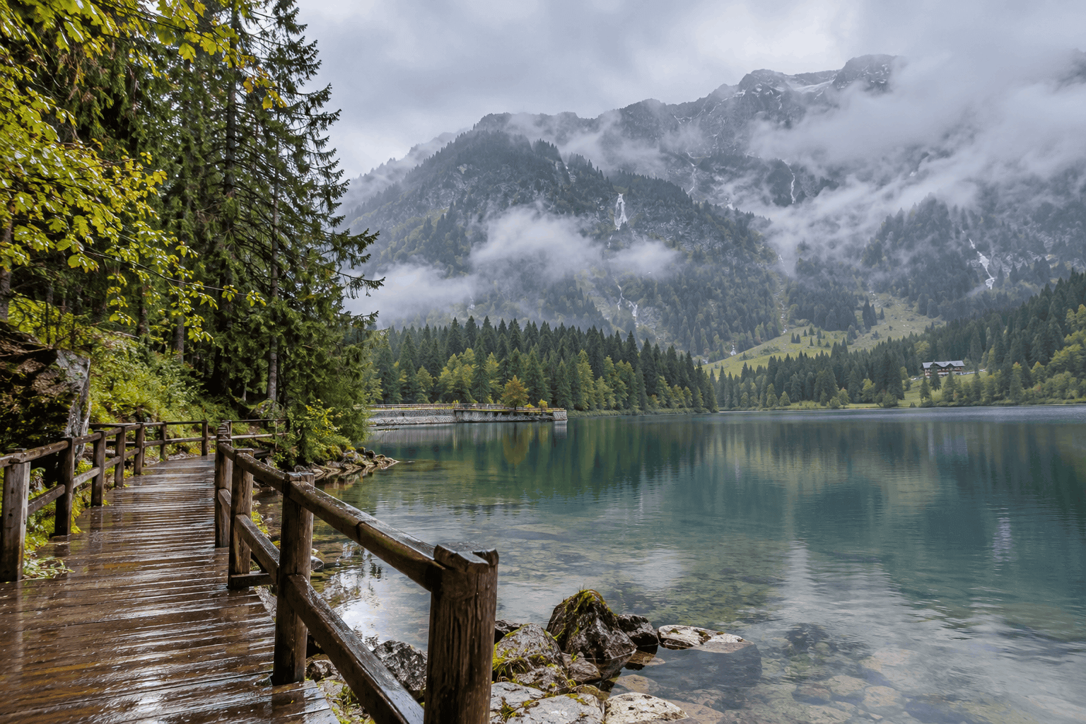 Wooden boardwalk along the shore of the Steirischer Bodensee with mist over the mountains