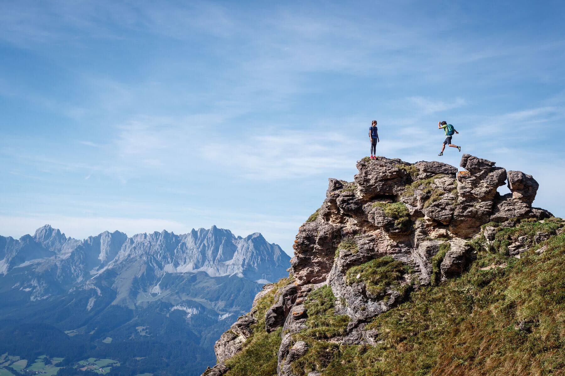 Twee wandelaars verkennen de Kitzbüheler Alpen op een rotsachtige top met uitzicht op de bergen.
