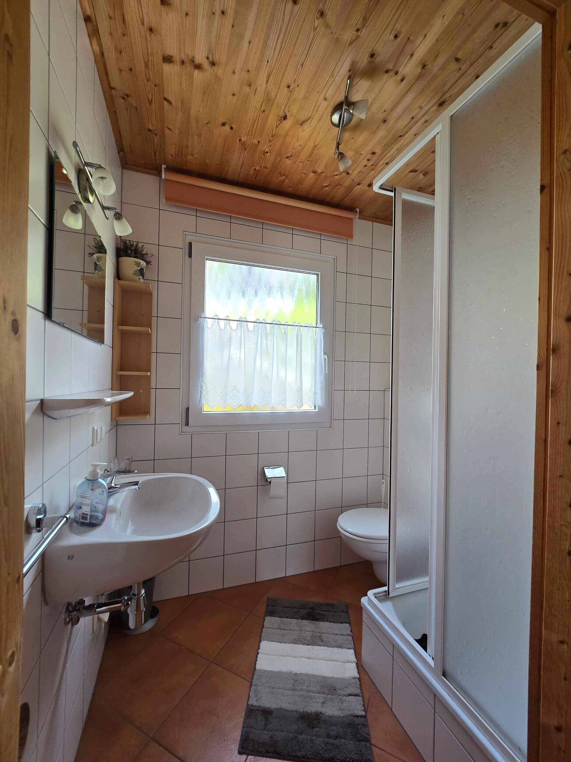Bathroom at Alpendorf Dachstein West with shower, washbasin, toilet and wooden ceiling.