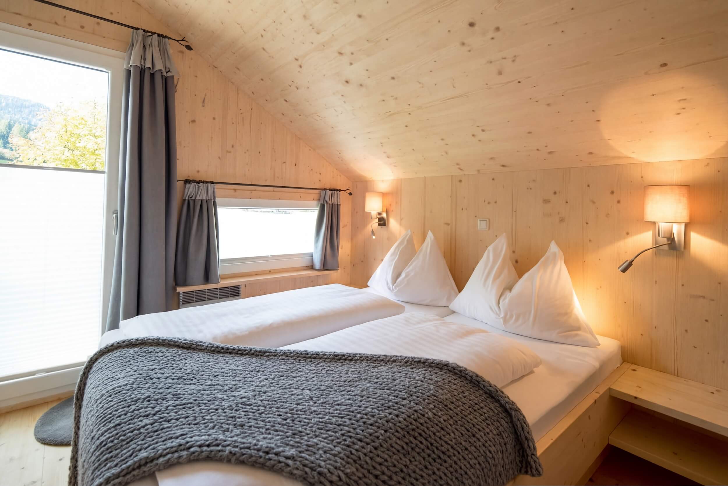 Cozy wooden bedroom with twin beds, soft blankets, and large windows showcasing a serene lakeside view.