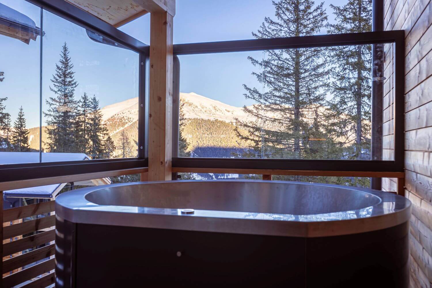 Außenbadewanne auf der Terrasse eines Chalets mit Blick auf die verschneiten Berge